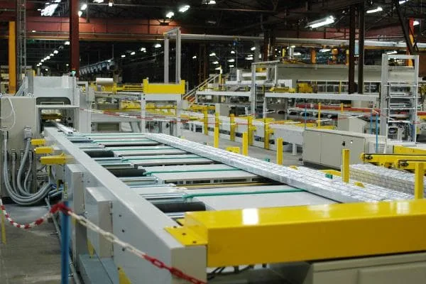 Automated aluminum extrusion handling line with yellow guard rails and roller conveyors on a factory floor