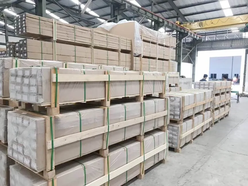 Stacked pallets of wood-framed and shrink-wrapped aluminum profile bundles in a warehouse under a gantry crane
