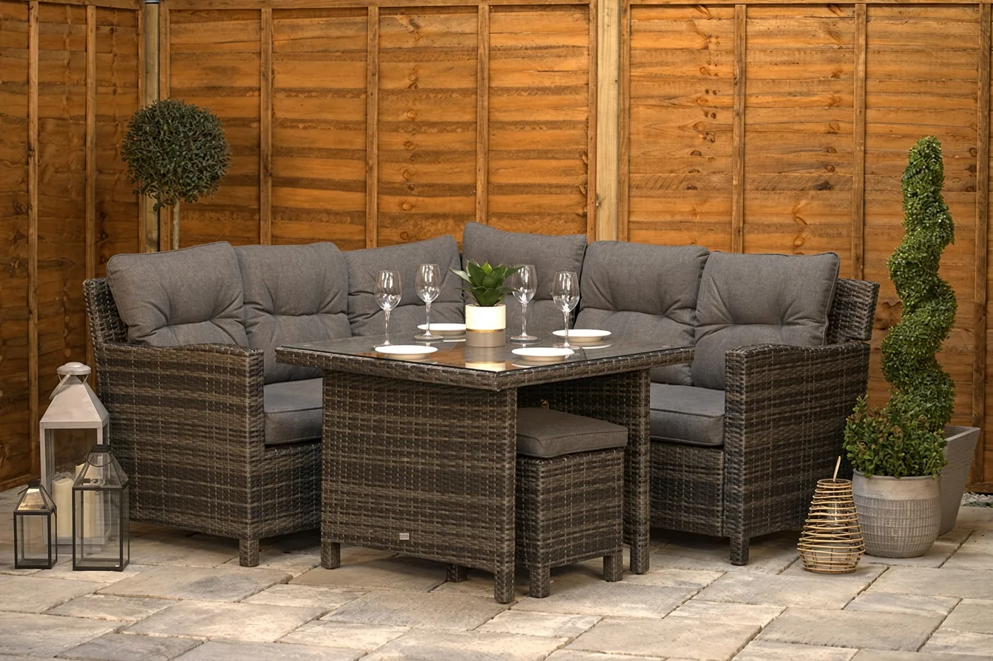Wicker garden sofa and coffee table set on a paved patio beside a wooden fence