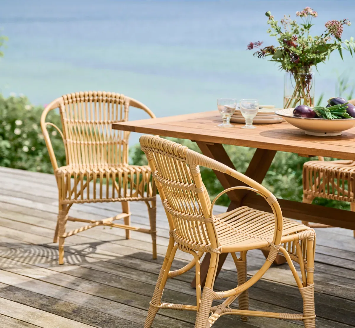 Lightweight woven outdoor dining chairs and a timber table on a waterside deck