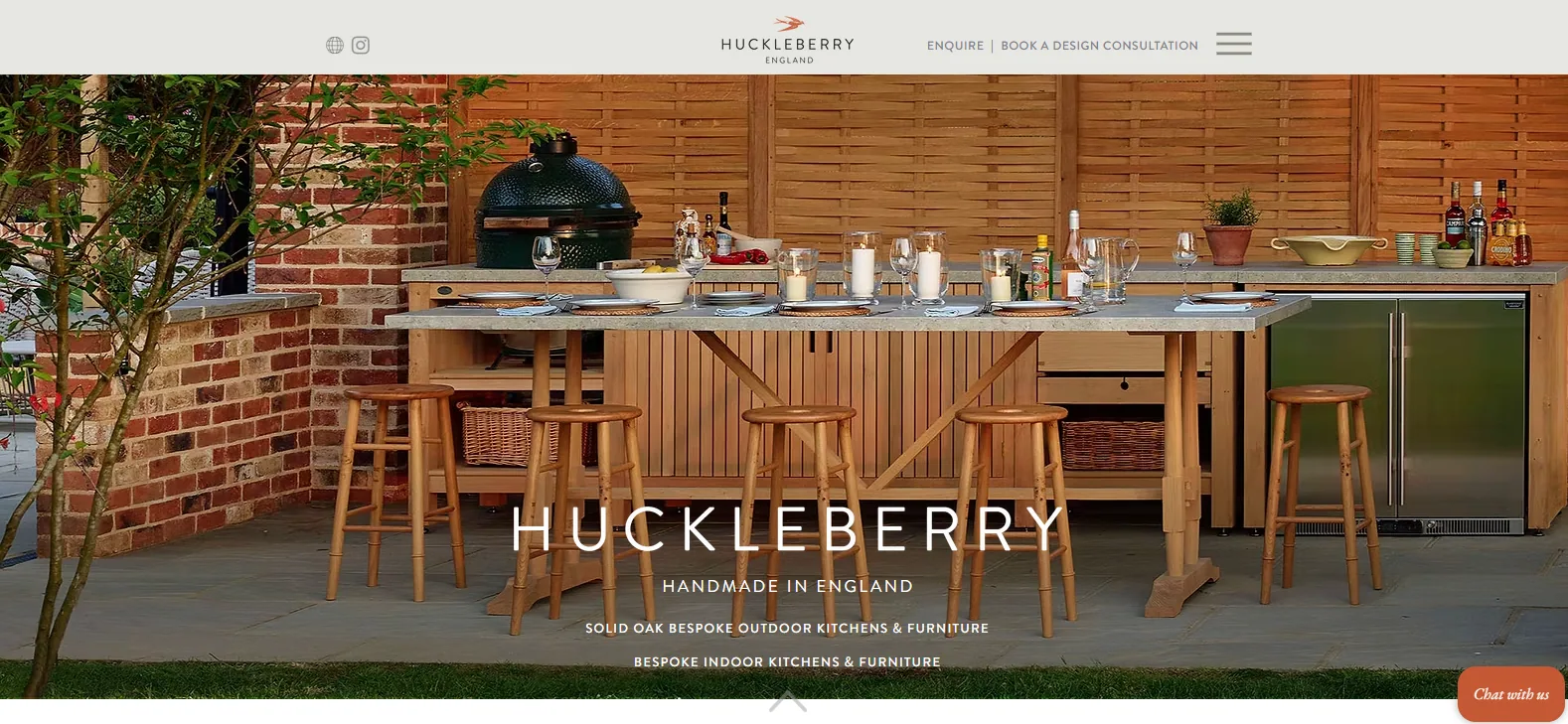 Huckleberry homepage showing a sheltered outdoor kitchen with timber cabinetry, a stone worktop, bar stools, a kamado grill and a brick back wall, headed Handmade in England