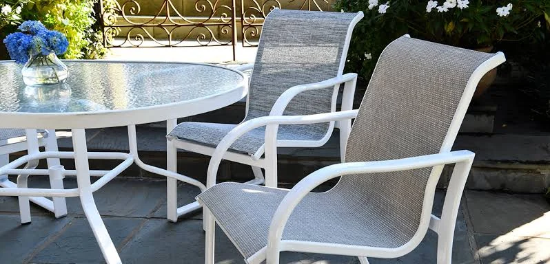 White sling-fabric armchairs around a round glass-top dining table on a slate patio
