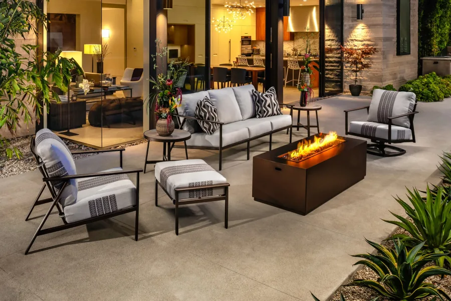 Dark steel-framed lounge seating with a linear fire table on a concrete patio at dusk