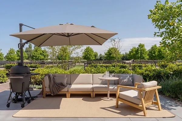 Outdoor furniture case study: a teak sectional sofa and armchair under a cantilever umbrella, beside a kamado charcoal grill on a residential patio
